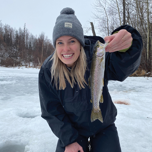 CORE employee, Caroline Van Horn, standing on ice and holding a fish
