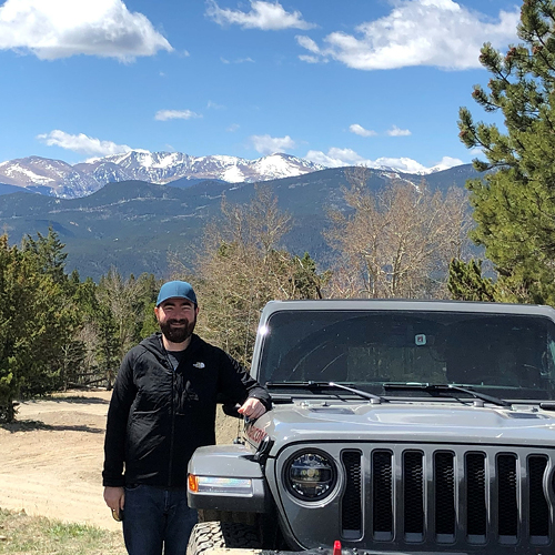 CORE employee next to a grey Jeep posing in front of the Rocky Mountains