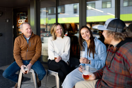 A group of two men and two women smiling and casually talking to one another, sitting outside